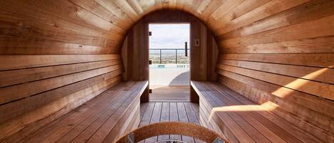 Una sauna con paredes y bancos de madera, vista a una piscina y cielo despejado.