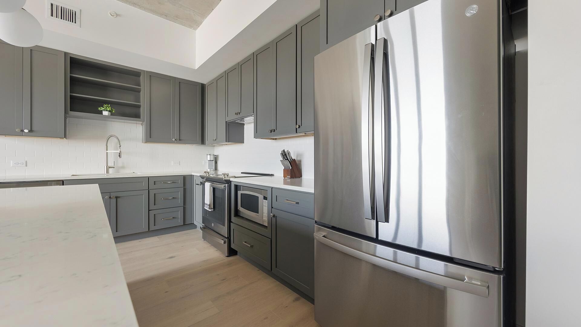 Una cocina moderna con gabinetes grises, electrodomésticos de acero inoxidable y piso de madera.