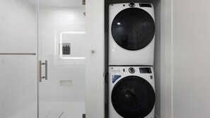 A laundry room with two stacked washing machines, a door, and a small window. - Landing | Spectacular 1BD, Yoga Studio, Gym (Denver)