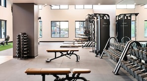 A gym with weightlifting equipment, benches, and a view of the city through large windows. - Landing | Spectacular 1BD, Yoga Studio, Gym (Denver)