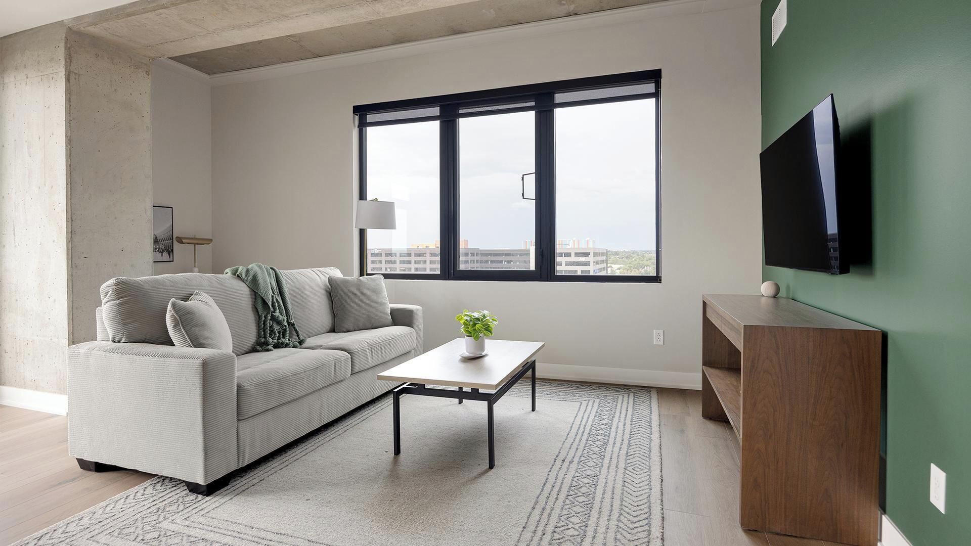 A modern living room with a sofa, coffee table, and a flat-screen TV mounted on a green wall.