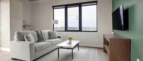 A modern living room with a sofa, coffee table, and a flat-screen TV mounted on a green wall.