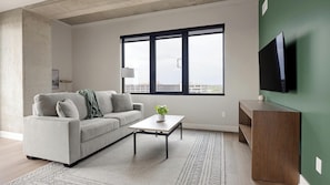 A modern living room with a sofa, coffee table, and a flat-screen TV mounted on a green wall. - Landing | Stunning 2BD, Clubhouse, Yoga Studio (Denver)