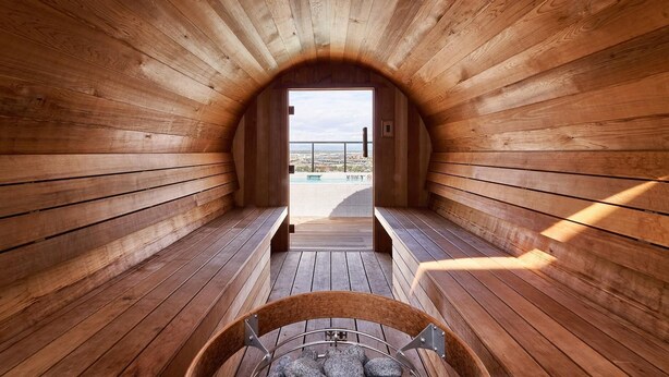 En sauna med trævægge og bænke, udsigt til en pool og en klar himmel.