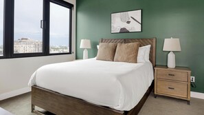 A bedroom with a large bed, two bedside tables with lamps, a view of the city through a window, and a piece of wall art above the bed. - Landing | Stunning 2BD, Clubhouse, Yoga Studio (Denver)