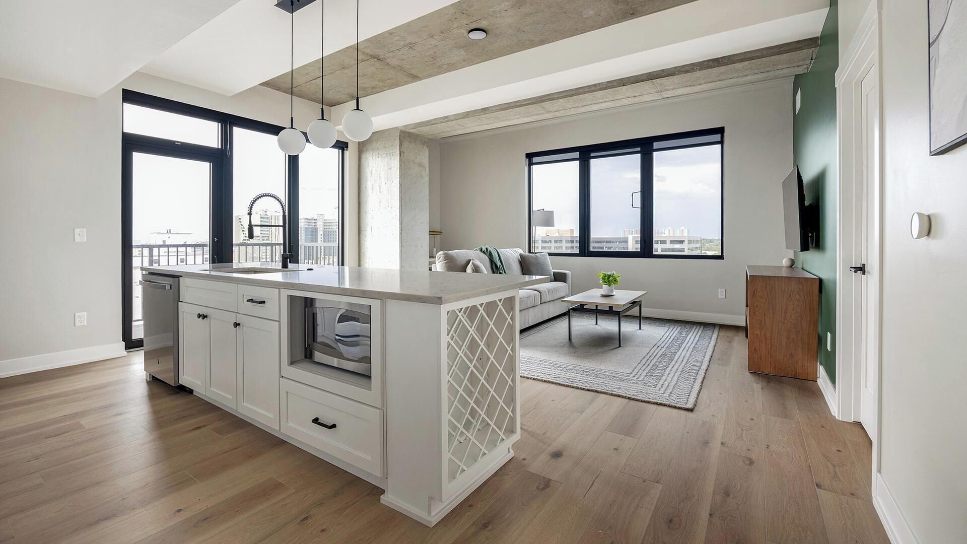 A modern kitchen with a central island, a dining area with a sofa and coffee table, and large windows offering a view of the city.