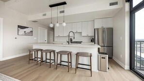 A modern kitchen with a central island, bar stools, stainless steel appliances, and a large window offering a view. - Landing | Stunning 2BD, Clubhouse, Yoga Studio (Denver)