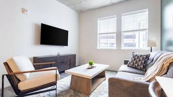 Un salon moderne avec un téléviseur à écran plat, un canapé, un fauteuil, une table basse et une petite plante.