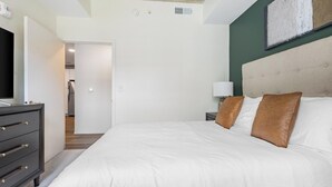 Une chambre à coucher comprenant un lit, une commode, une table de chevet et une œuvre d’art accrochée au mur.