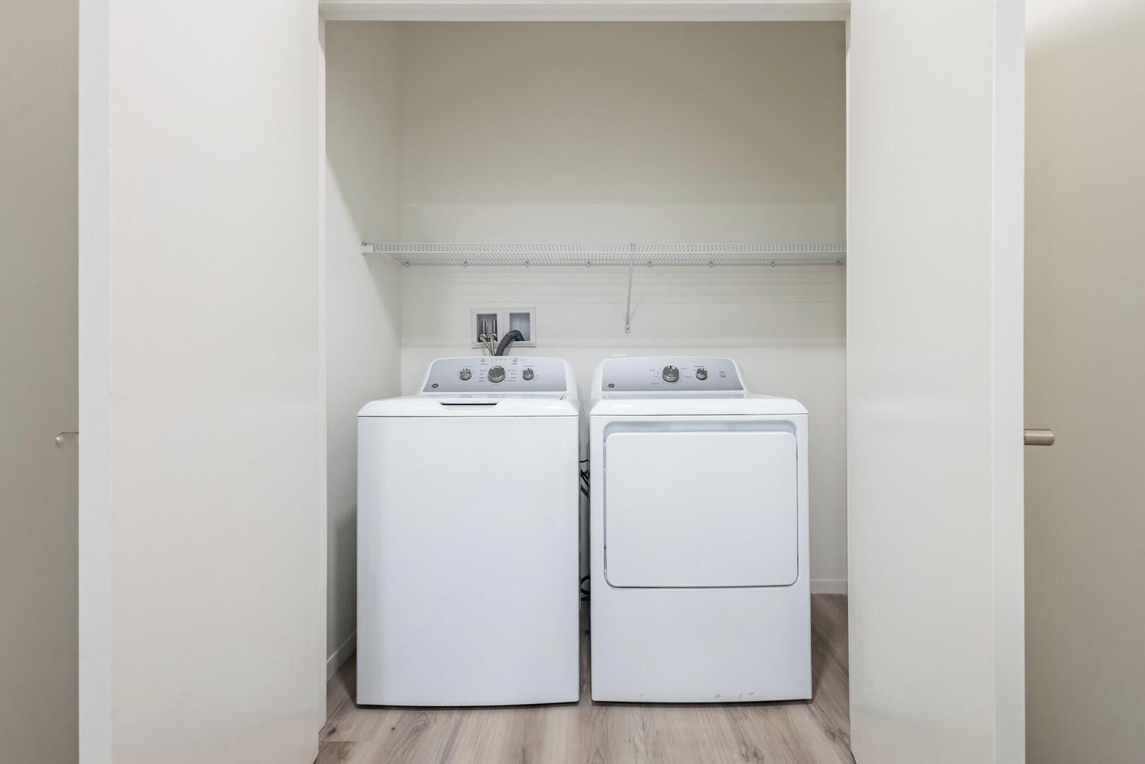 Une buanderie équipée de deux machines à laver à chargement frontal, de couleur blanche, et d’une étagère en métal placée au-dessus.
