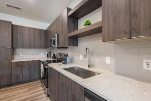 A modern kitchen with dark wood cabinets, a stainless steel sink, and a built-in microwave. - Landing | Incredible 2BD in Steelpointe Harbor (Bridgeport)