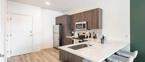 A modern kitchen with a central island, stainless steel appliances, and bar stools.
