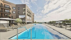 Ein Schwimmbecken mit Liegestühlen und ein modernes Gebäude mit Balkonen.