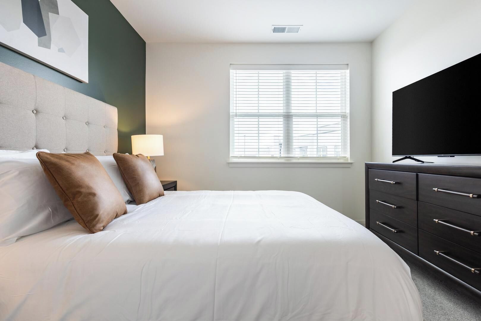 Une chambre d’hôtel avec un lit, une télévision, une fenêtre avec des stores et une commode.