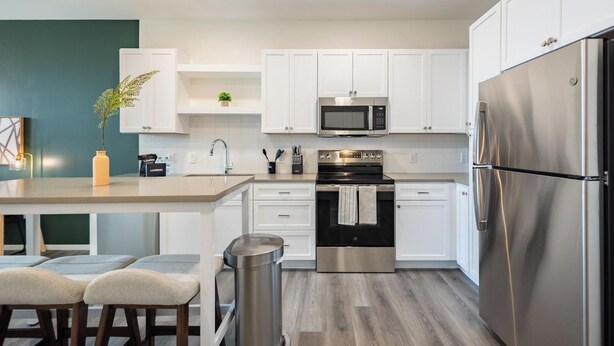 A modern kitchen with white cabinets, stainless steel appliances, and a central island with seating. - Landing | Chic 1BD in Steelpointe Harbor (Bridgeport)