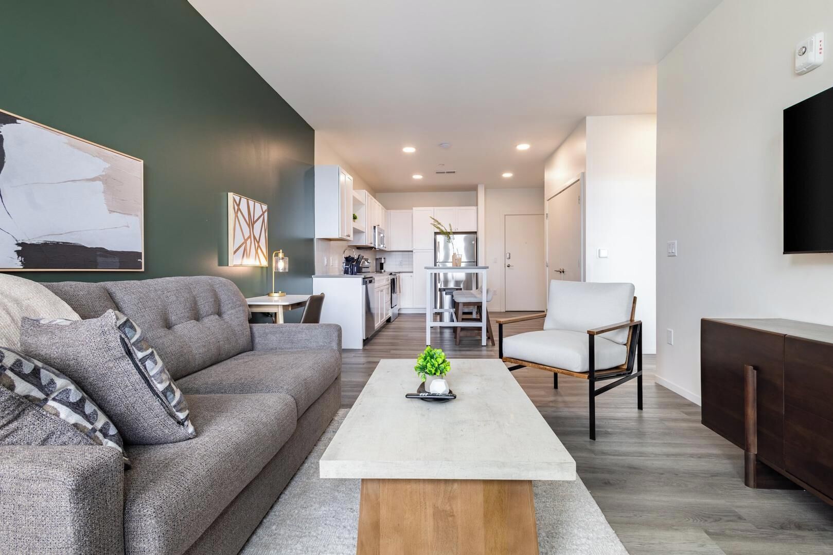 Un salon moderne avec un canapé gris, une table basse et un téléviseur fixé au mur.