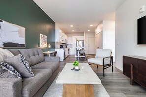 A modern living room with a grey sofa, a coffee table, and a TV mounted on the wall. - Landing | Chic 1BD in Steelpointe Harbor (Bridgeport)