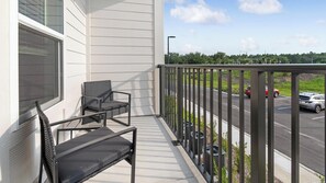 A balcony with two chairs, a view of a road with cars, and a street lamp. - Landing | Beautiful 2BD, Gym (St. Augustine)