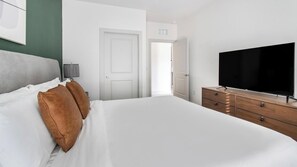 A hotel room with a large bed, a TV, a dresser, and a door leading to another room. - Landing | Amazing 2BD, Gym (St. Augustine)