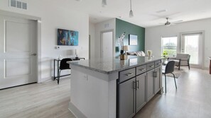 A modern kitchen with a central island, a dining area with a table and chairs, and a view of the outdoors. - Landing | Amazing 2BD, Gym (St. Augustine)
