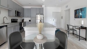 A modern kitchen with grey cabinets, a central island, and a dining area with two chairs. - Landing | Beautiful 2BD, Gym (St. Augustine)
