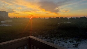 Een zonsondergang boven een landschap met heldere lucht, een gebouw in de verte en een weg op de voorgrond.