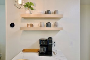 Une cuisine équipée d’une machine à café, d’une plante et d’étagères remplies de tasses.