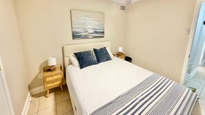 Een slaapkamer met een bed, nachtkastje, plafondventilator en een schilderij aan de muur.
