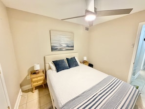 Ein Schlafzimmer mit einem Bett, einem Nachttisch, einem Deckenventilator und einem Bild an der Wand.