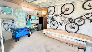 Een garage met fietsen aan de muur, een blauwe kar en diverse spullen op planken.