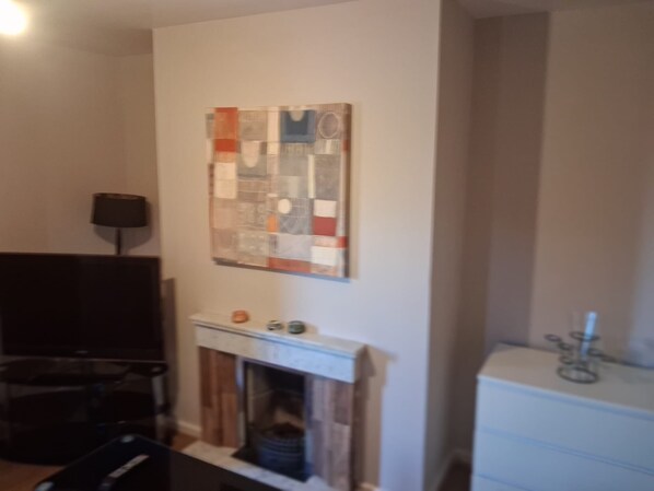 A living room with a fireplace, a flat-screen TV, and a wall-mounted artwork.
