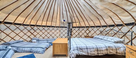 A yurt interior with a bed, wooden furniture, and a central support pole.