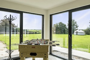 Ein Fußballtisch in einem Raum mit großen Fenstern und Blick auf eine Wiese.