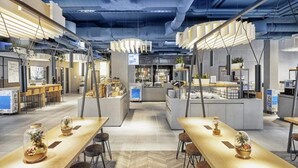 Moderni ravintola, jossa on korkeat katot, esillä olevat ilmastointiputket ja keskeinen tarjoilualue.