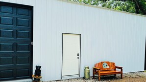 A building with a black garage door, a white door, and a bench with a bear decoration. - Cozy 1-bedroom garage apartment in pleasant Hot Springs National Park, (Hot Springs)