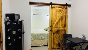 A compact room with a bed, a small table with chairs, a refrigerator, and a wooden sliding door. - Cozy 1-bedroom garage apartment in pleasant Hot Springs National Park, (Hot Springs)