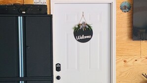 A white door with a 'Welcome' sign, a clock, and a small figurine on the wall. - Cozy 1-bedroom garage apartment in pleasant Hot Springs National Park, (Hot Springs)