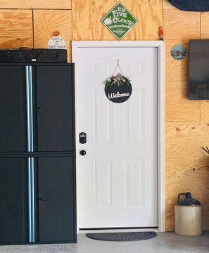 Eine weiße Tür mit einem 'Welcome'-Schild, einer Uhr und einer kleinen Figur an der Wand.