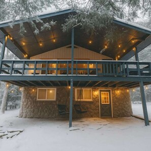 Eine zweistöckige Holzhütte mit Balkon, Steinmauern und einer Holzterrasse.