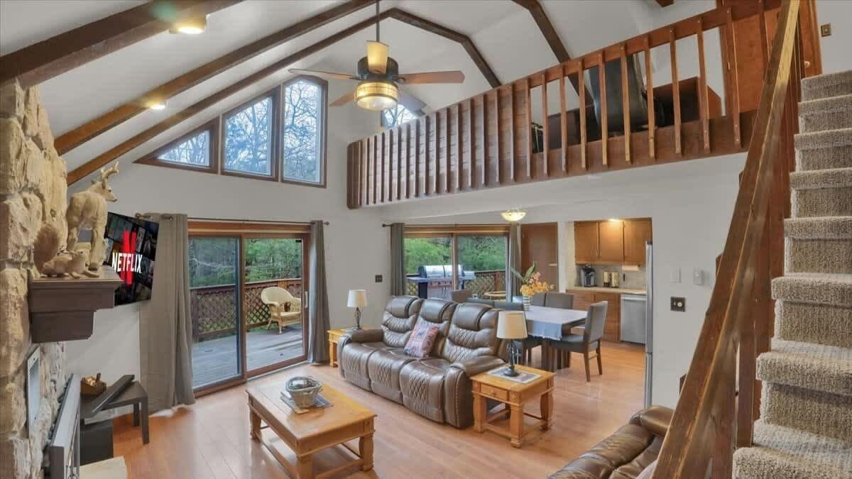 A spacious loft-style living area with a high ceiling, a leather sofa, a dining table, and a staircase leading to an upper level.
