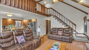 Ein geräumiger Wohnbereich mit Ledersofas, einer Holztreppe und einer Küche im Hintergrund.
