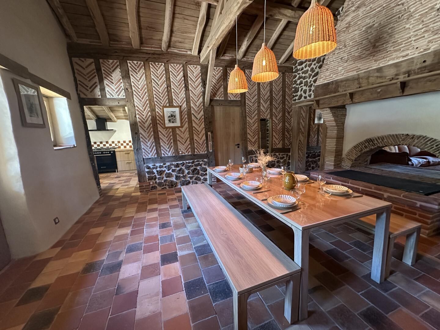A rustic dining area with a long wooden table, benches, and hanging wicker lamps.