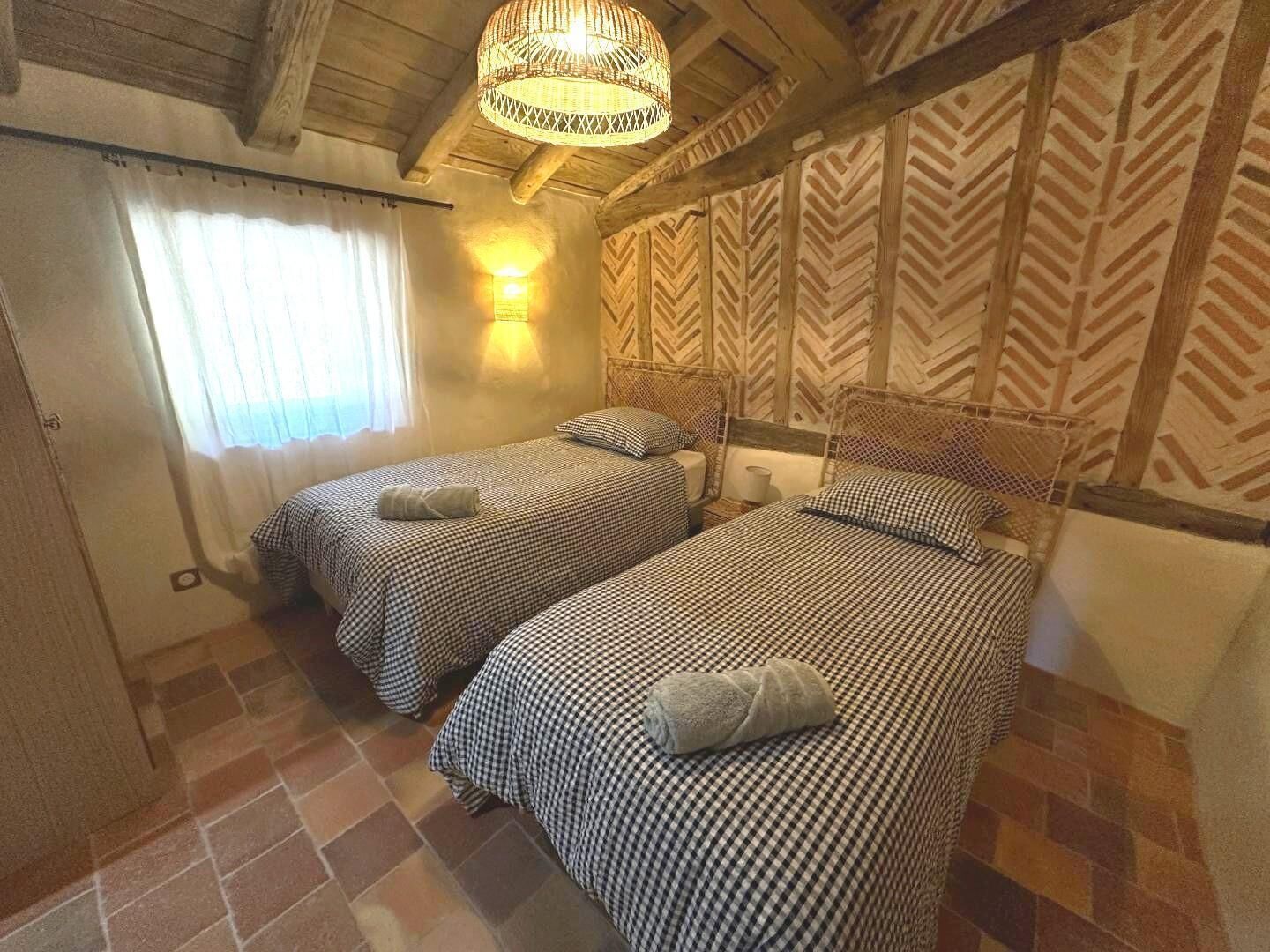 Een kamer met twee bedden, een raam met gordijnen, een wandlamp en een behang met patroon.