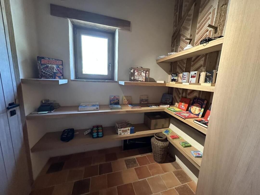 En smal gang med reoler fyldt med bøger og kasser, et vindue samt et flisegulv.