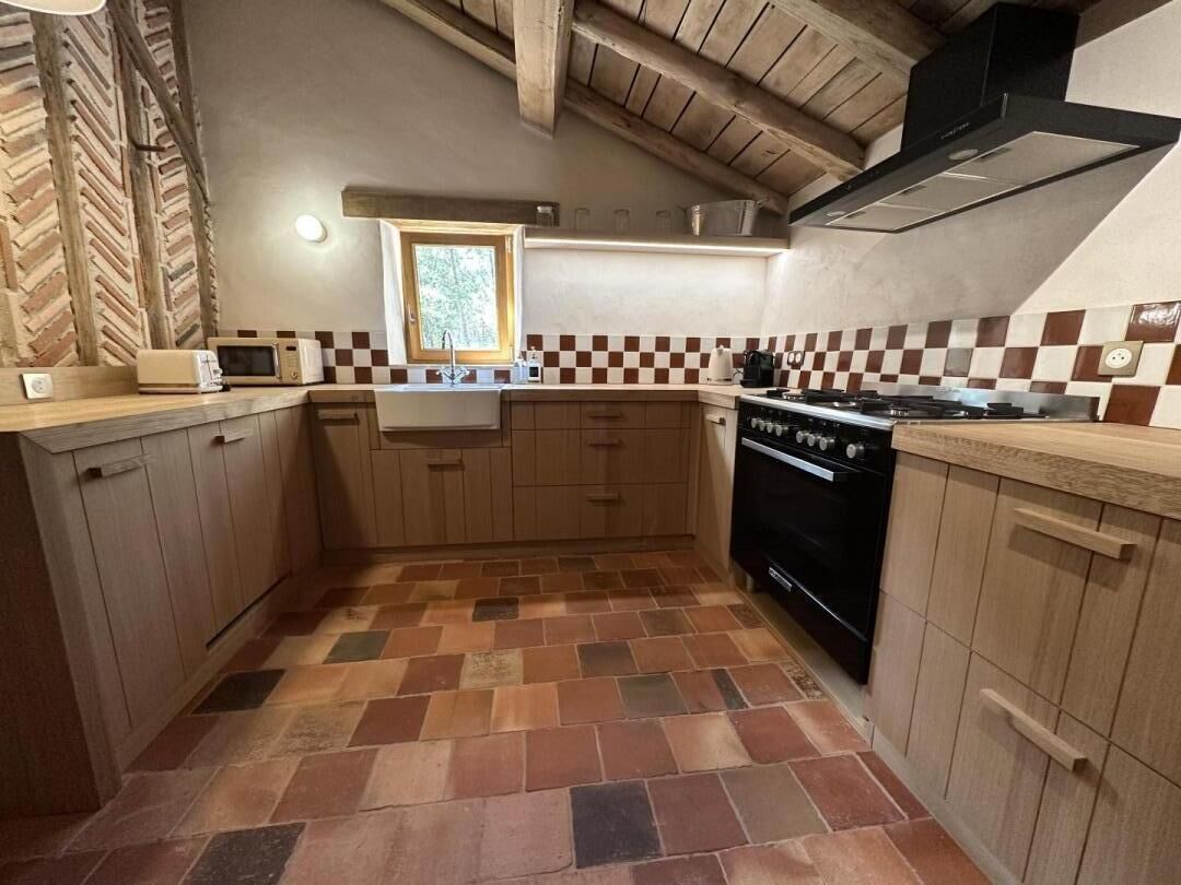 A compact kitchen with wooden cabinets, a tiled floor, a microwave, a stove, and a window.