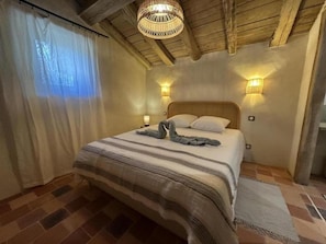 Ein Schlafzimmer mit einem Bett, einer gewebten Deckenleuchte, Wandleuchten und einem Fenster mit Vorhängen.