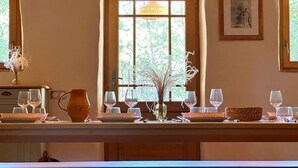 A dining area with a wooden table set for a meal, a window with a view of trees, and a framed picture on the wall. - La Landaise - COMMENSACQ (COMMENSACQ)