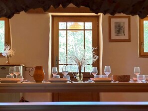Ein Essbereich mit Holztisch, gedeckt für eine Mahlzeit, einem Fenster mit Blick auf Bäume und einem gerahmten Bild an der Wand.