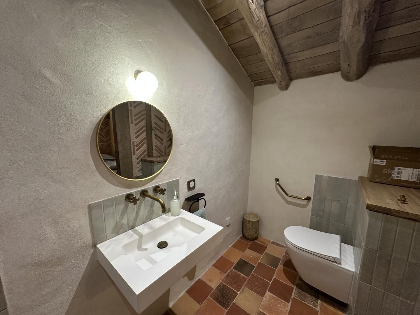 A bathroom with a white sink, a round mirror, a toilet, and a wooden ceiling.