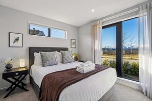 A modern hotel room with a large bed, a bedside table with a lamp, and a view of a mountainous landscape. - Base Northlake | Peaceful with Mountain Views (Wānaka)